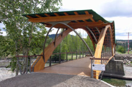 The Bridge of Dreams spans the Tulameen River in Princeton, B.C., Canada.  The wooden foot-bridge deck is suspended by steel rods from glulam arches and is covered by an undulating steel roof deck built on sawn timber purlins.  Design/Build by StructureCraft Builders, Inc.  (Photo courtesy StructureCraft Builders, Inc.)