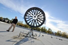 The wind turbine installed on top of SCU’s facilities building is being monitored for its effectiveness and energy production output.  Mr. Joe Sugg, Assistant Vice President of University Operations of Santa Clara University, gives scale to the size of the wind turbine.  (Photo courtesy Santa Clara University)