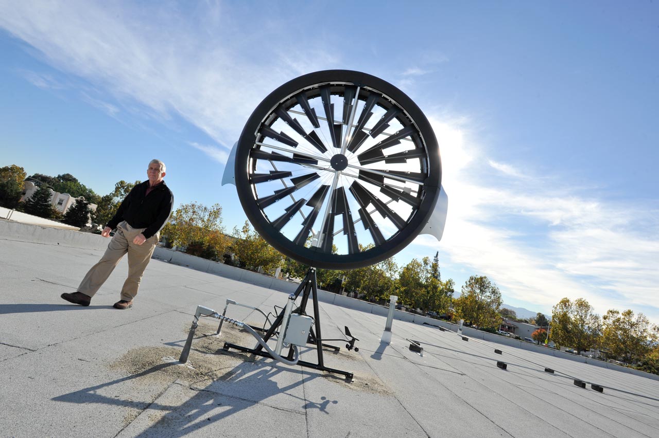 The wind turbine installed on top of SCU’s facilities building is being monitored for its effectiveness and energy production output.  Mr. Joe Sugg, Assistant Vice President of University Operations of Santa Clara University, gives scale to the size of the wind turbine.  (Photo courtesy Santa Clara University)